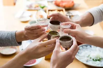 5 people cheering with glasses of sake over a table