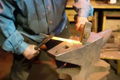 A blacksmith using a hammer and an anvil.