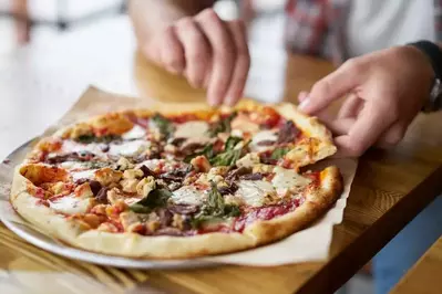 Hands pulling a slice from a delicious pizza with chicken and spinach.